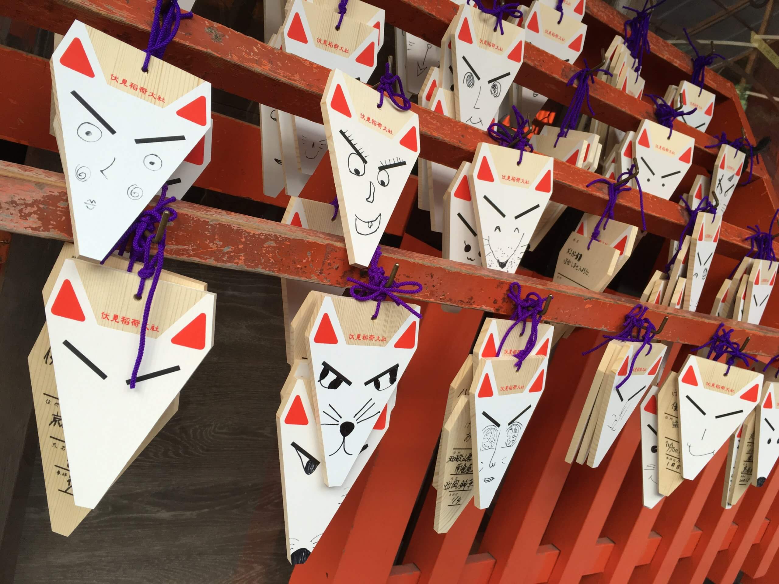 Fox-shaped wooden prayer plaques with drawn faces at Fushimi Inari Taisha in Kyoto