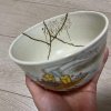 Japanese tea bowl repaired with kintsugi, showing gold-filled cracks and a colorful illustration of the Tenjin Matsuri, an annual festival in Osaka, on the front
